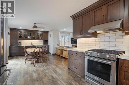 Kitchen with stainless steel appliances, dark wood finish cabinets, glass insert cabinets, dark wood-style floors, and decorative backsplash - 23247 Beattie Line, Elgin, ON - Indoor Photo Showing Kitchen