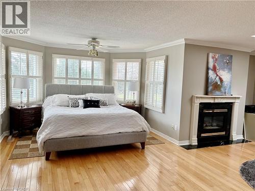 Bedroom with crown molding, light wood finished floors, a fireplace with flush hearth, a textured ceiling, and a ceiling fan - 2056 Hadfield Court, Burlington, ON - Indoor Photo Showing Bedroom With Fireplace
