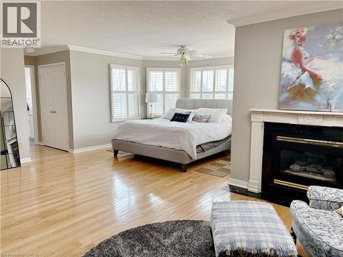 Bedroom with crown molding, light wood finished floors, a fireplace with flush hearth, a textured ceiling, and a closet - 2056 Hadfield Court, Burlington, ON - Indoor Photo Showing Bedroom With Fireplace