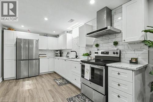 Kitchen featuring stainless steel appliances, range hood, white cabinetry, light wood-style floors, and light stone countertops - 284 Normanhurst Avenue, Hamilton, ON - Indoor Photo Showing Kitchen With Upgraded Kitchen