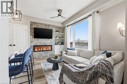 Living area featuring a ceiling fan, built in features, light wood-style flooring, and a stone fireplace - 