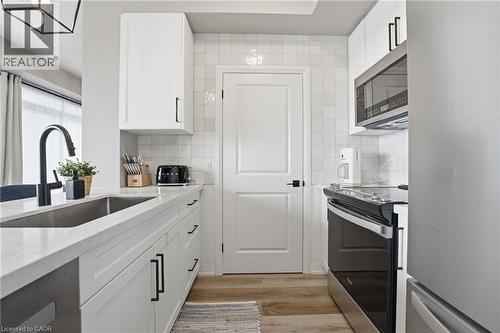 Kitchen featuring stainless steel appliances, white cabinets, light stone countertops, and light wood-type flooring - 120 Springvalley Crescent Unit# 203, Hamilton, ON - Indoor Photo Showing Kitchen With Upgraded Kitchen