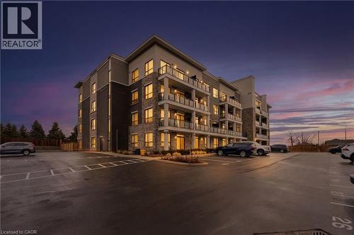 Property at dusk with a view of apartment building / complex and uncovered parking - 120 Springvalley Crescent Unit# 203, Hamilton, ON - Outdoor With Facade