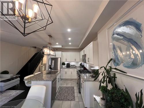 Kitchen with a chandelier, a tray ceiling, stainless steel appliances, dark stone countertops, and an island with sink - 1165 West 5Th Street, Hamilton, ON - Indoor Photo Showing Other Room