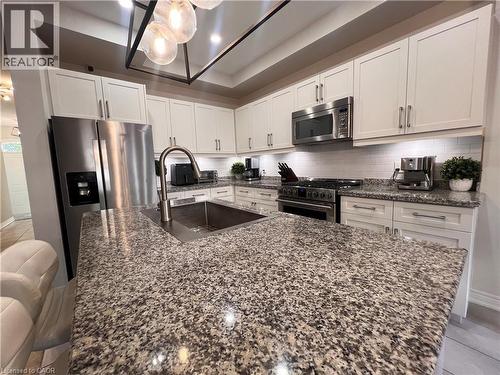 Kitchen with dark stone counters, stainless steel appliances, white cabinetry, a center island with sink, and decorative backsplash - 1165 West 5Th Street, Hamilton, ON - Indoor Photo Showing Kitchen With Upgraded Kitchen