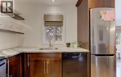 Kitchen with freestanding refrigerator, black dishwasher, light stone counters, open shelves, and wood finish cabinets - 