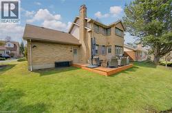 Back of property featuring a deck, brick siding, a chimney, a lawn, and roof with shingles - 