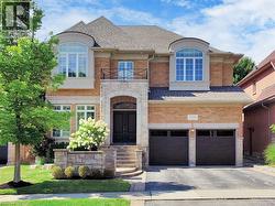 French country inspired facade featuring a shingled roof, stone siding, a garage, a balcony, and driveway - 