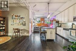 Kitchen with open floor plan, a breakfast bar, stainless steel appliances, cream cabinets, and dark wood-type flooring - 