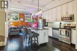 Kitchen featuring stainless steel appliances, open floor plan, a kitchen breakfast bar, dark wood-style floors, and white cabinetry - 