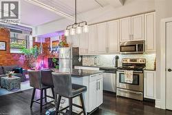 Kitchen with stainless steel appliances, dark stone counters, a breakfast bar, dark wood finished floors, and white cabinets - 