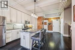 Kitchen with stainless steel appliances, dark stone counters, brick wall, a breakfast bar, and white cabinets - 