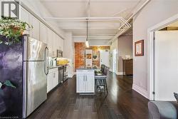 Kitchen featuring stainless steel appliances, white cabinets, dark wood finished floors, a breakfast bar area, and decorative light fixtures - 