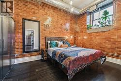 Bedroom with dark wood-style floors, freestanding refrigerator, and brick wall - 
