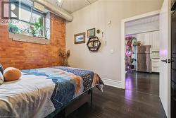 Bedroom featuring brick wall, dark wood finished floors, and freestanding refrigerator - 