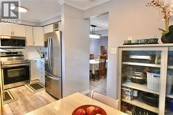 Kitchen featuring stainless steel appliances, ornamental molding, white cabinetry, light wood-style flooring, and pendant lighting - 