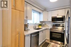 Kitchen with stainless steel appliances, ornamental molding, light stone counters, light wood-style floors, and white cabinets - 