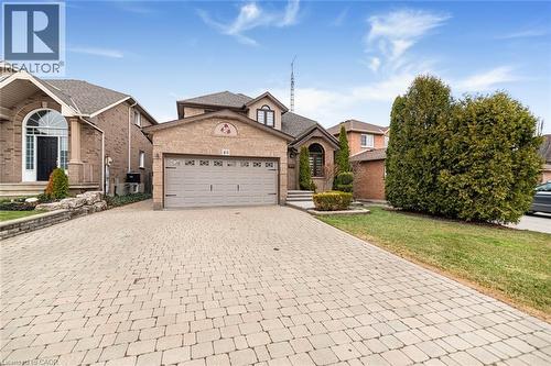 View of front of property with an attached garage, decorative driveway, brick siding, and a front lawn - 40 Artistic Boulevard, Hamilton, ON - Outdoor With Facade