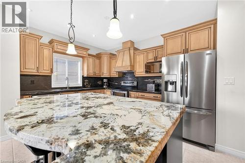 Kitchen featuring stainless steel appliances, a kitchen bar, potlights, pendant lighting, a center island, and light stone countertops - 182 Irwin Avenue, Hamilton, ON - Indoor Photo Showing Kitchen