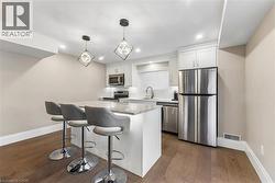 Kitchen with stainless steel appliances, white cabinetry, light stone counters, dark wood-style floors, and a kitchen breakfast bar - 