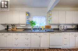 Kitchen with dark countertops, white dishwasher, open shelves, and white cabinetry - 