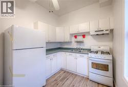 Kitchen with white appliances, light wood-style floors, white cabinets, ceiling fan, and dark countertops - 