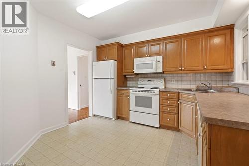 Kitchen with white appliances, wood finish cabinetry, light flooring, and tasteful backsplash - 890 Falcon Boulevard, Burlington, ON - Indoor Photo Showing Kitchen With Double Sink