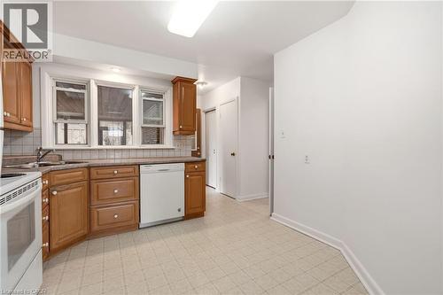 Kitchen with white appliances, wood finish cabinetry, backsplash, and light floors - 890 Falcon Boulevard, Burlington, ON - Indoor Photo Showing Kitchen With Double Sink