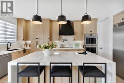 Kitchen with light wood finish cabinetry, light stone counters, stainless steel appliances, and a center island with sink - 