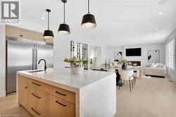 Kitchen featuring light wood finish cabinets, light wood-type flooring, light stone countertops, built in fridge, and a center island with sink - 