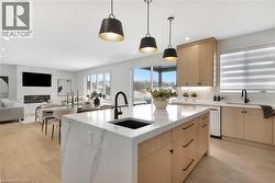 Kitchen with light wood finish cabinets, light wood finished floors, light stone countertops, and a center island with sink - 