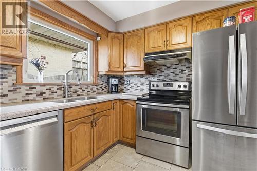 Kitchen featuring stainless steel appliances, light tile patterned floors, wood finish cabinets, light stone countertops, and decorative backsplash - 135 Burbank Road, Kitchener, ON - Indoor Photo Showing Kitchen With Double Sink