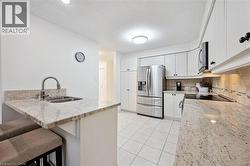 Kitchen with light stone countertops, appliances with stainless steel finishes, white cabinetry, a peninsula, and a kitchen breakfast bar - 
