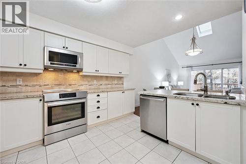 Kitchen with a skylight, appliances with stainless steel finishes, vaulted ceiling, white cabinetry, and pendant lighting - 92 Schroder Crescent, Guelph, ON - Indoor Photo Showing Kitchen With Double Sink