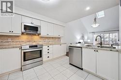 Kitchen with a skylight, appliances with stainless steel finishes, vaulted ceiling, white cabinetry, and pendant lighting - 