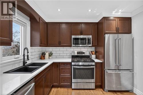 Kitchen with stainless steel appliances, ornamental molding, light wood-style floors, decorative backsplash, and dark wood finish cabinets - 248 London Street S, Hamilton, ON - Indoor Photo Showing Kitchen With Double Sink