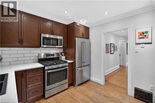 Kitchen with stainless steel appliances, tasteful backsplash, dark wood finish cabinetry, light wood-style flooring, and recessed lighting - 248 London Street S, Hamilton, ON - Indoor Photo Showing Kitchen