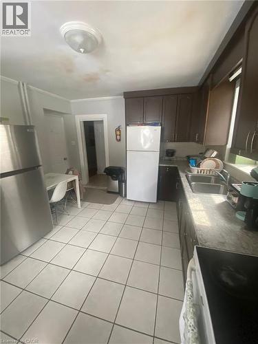 Kitchen with white appliances, dark wood finish cabinets, light tile patterned floors, light countertops, and ornamental molding - 9 Waterloo Avenue, Guelph, ON - Indoor Photo Showing Kitchen With Double Sink