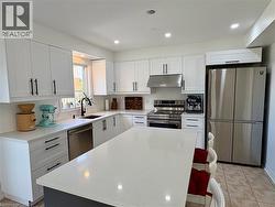 Kitchen featuring a large island with white countertop, white cabinetry with black hardware, stainless steel appliances, and recessed lighting - 