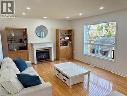 Living area featuring a white mantel fireplace with a gas insert, recessed lighting, wood-finish flooring, and a large window overlooking exterior greenspace - 