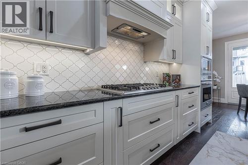 Kitchen featuring dark stone counters, dark wood-style flooring, white cabinetry, stainless steel appliances, and backsplash - 2719 Torrey Pines Way, London, ON - Indoor Photo Showing Kitchen With Upgraded Kitchen