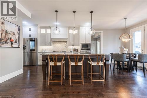 Dual tone kitchen featuring stainless steel appliances, two tone cabinets, an island with sink, dark wood-type flooring, and a breakfast bar - 2719 Torrey Pines Way, London, ON - Indoor
