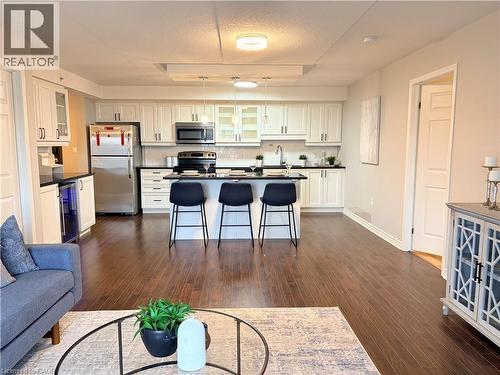 Kitchen featuring glass insert cabinets, dark countertops, stainless steel appliances, white cabinetry, and a kitchen breakfast bar - 776 Laurelwood Drive Unit# 406, Waterloo, ON - Indoor Photo Showing Kitchen