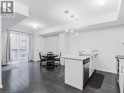 Kitchen featuring white cabinetry, a peninsula, dark wood finished floors, hanging light fixtures, and light stone countertops - 1206 Main Street E Unit# 113, Milton, ON - Indoor Photo Showing Other Room