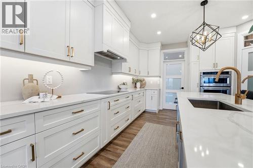 Kitchen featuring white cabinetry, light stone countertops, stainless steel double oven, dark wood-type flooring, and suspended lighting - 39 Mill Race Crescent, St. Jacobs, ON - Indoor Photo Showing Kitchen With Upgraded Kitchen