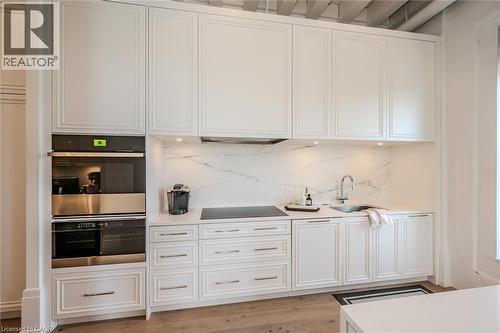 Kitchen featuring stainless steel double oven, white cabinetry, decorative backsplash, light wood-style floors, and black electric cooktop - 19 Guelph Avenue Unit# 308, Cambridge, ON - Indoor Photo Showing Other Room