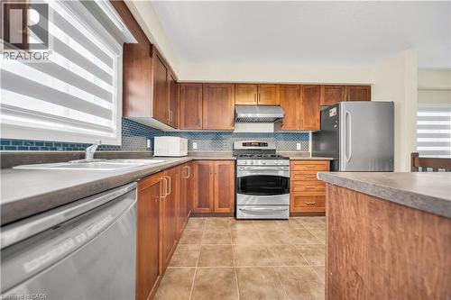 Kitchen featuring stainless steel appliances, wood finish cabinetry, light tile patterned flooring, tasteful backsplash, and light countertops - 51 Seabrook Drive, Kitchener, ON - Indoor Photo Showing Kitchen With Double Sink