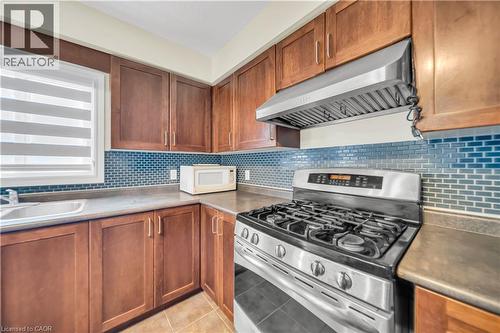 Kitchen with stainless steel range with gas stovetop, light tile patterned flooring, wood finish cabinetry, and white microwave - 51 Seabrook Drive, Kitchener, ON - Indoor Photo Showing Kitchen