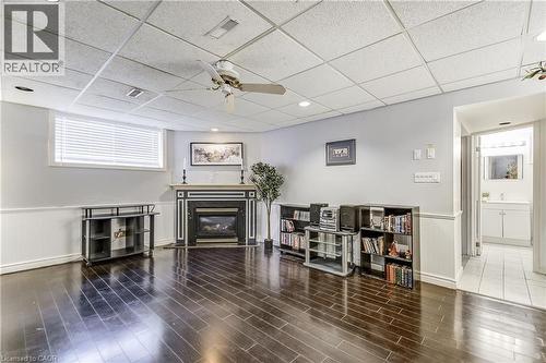 Living room with a wainscoted wall, a drop ceiling, a glass covered fireplace, a ceiling fan, and wood finished floors - 2145 Sandringham Drive, Burlington, ON - Indoor Photo Showing Other Room With Fireplace