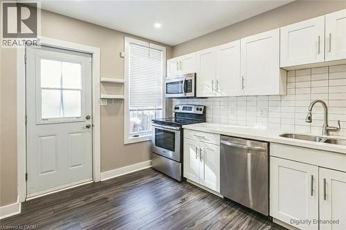 Kitchen with stainless steel appliances, white cabinetry, dark wood-style floors, backsplash, and light stone counters - 27 Ashley Street, Hamilton, ON - Indoor Photo Showing Kitchen With Stainless Steel Kitchen With Double Sink